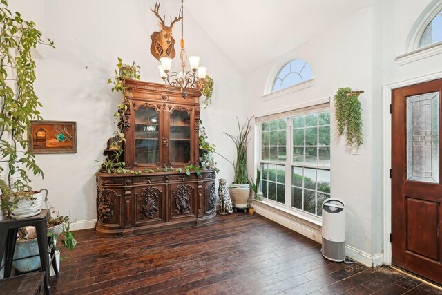 foyer entrance featuring dark wood-type flooring, baseboards, high vaulted ceiling, and a chandelier