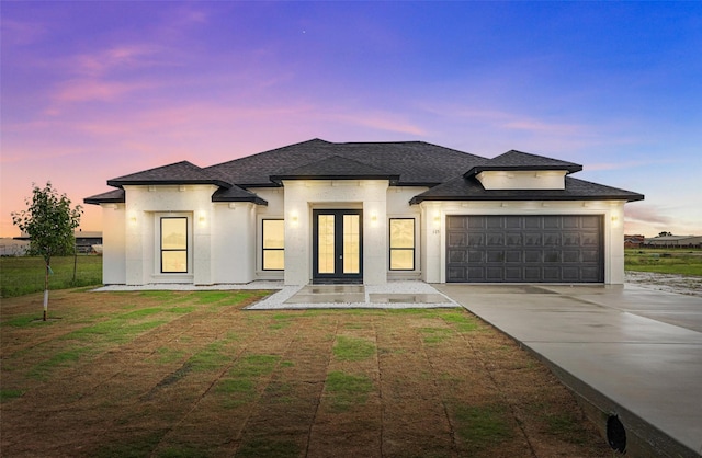 french country inspired facade featuring french doors, driveway, an attached garage, stucco siding, and roof with shingles