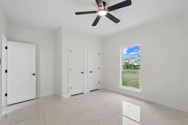 unfurnished bedroom featuring light marble finish floors, baseboards, and a ceiling fan