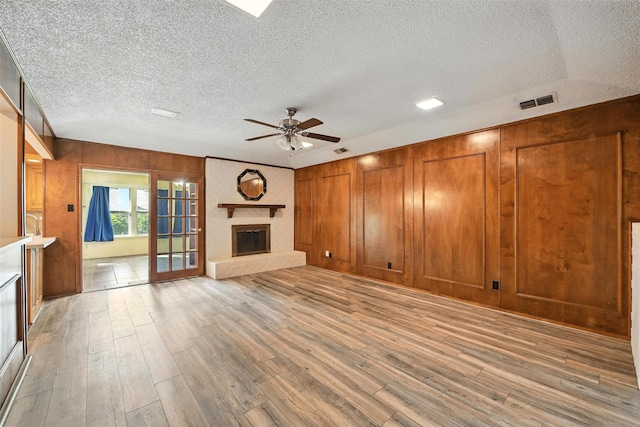 3908 Windhaven Rd, Fort Worth, TX 76133 - unfurnished living room with a glass covered fireplace, a ceiling fan, wood walls, light wood-style flooring, and a textured ceiling
