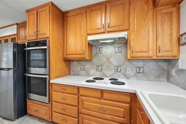 3908 Windhaven Rd, Fort Worth, TX 76133 - kitchen with stainless steel appliances, light countertops, brown cabinets, decorative backsplash, and under cabinet range hood