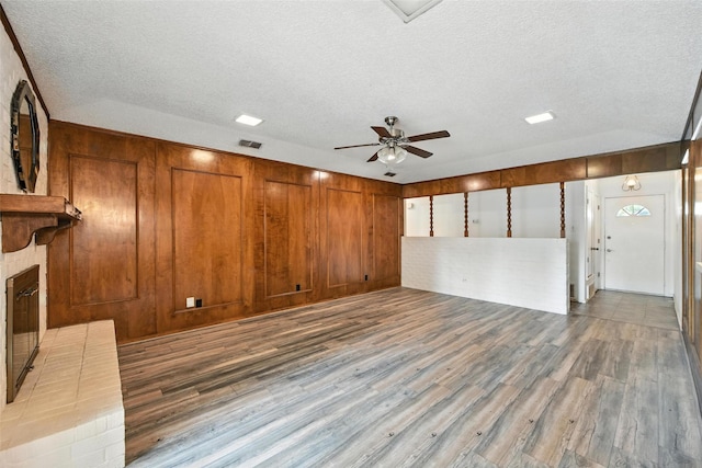 3908 Windhaven Rd, Fort Worth, TX 76133 - unfurnished living room with wood finished floors, a textured ceiling, a ceiling fan, a brick fireplace, and wood walls