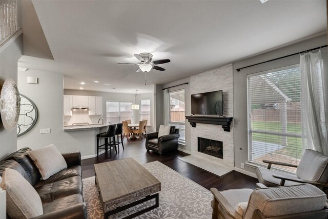 living room featuring a ceiling fan, baseboards, dark wood-style flooring, recessed lighting, and a stone fireplace