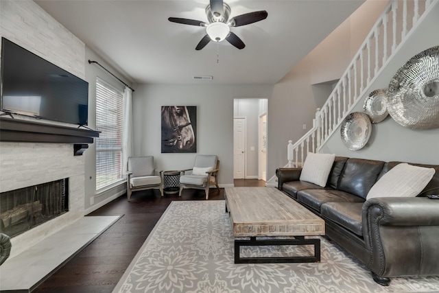 living room with stairway, a ceiling fan, a stone fireplace, wood finished floors, and baseboards