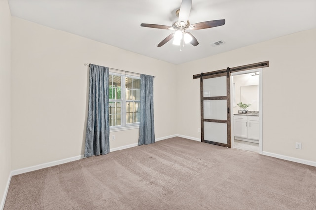 unfurnished room featuring a barn door, light carpet, a ceiling fan, and baseboards