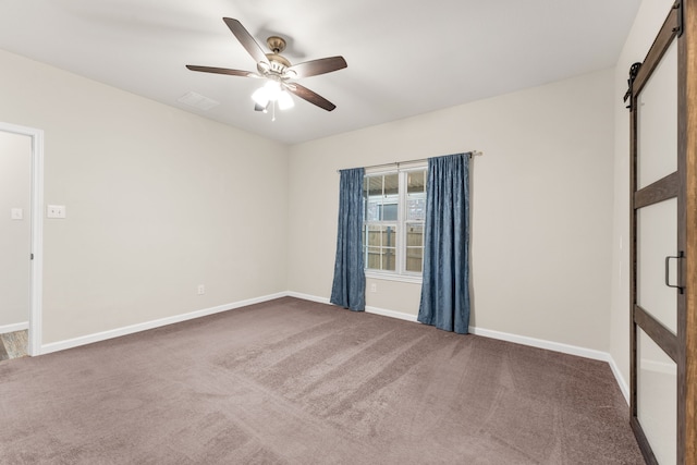 carpeted empty room with a barn door, baseboards, and ceiling fan