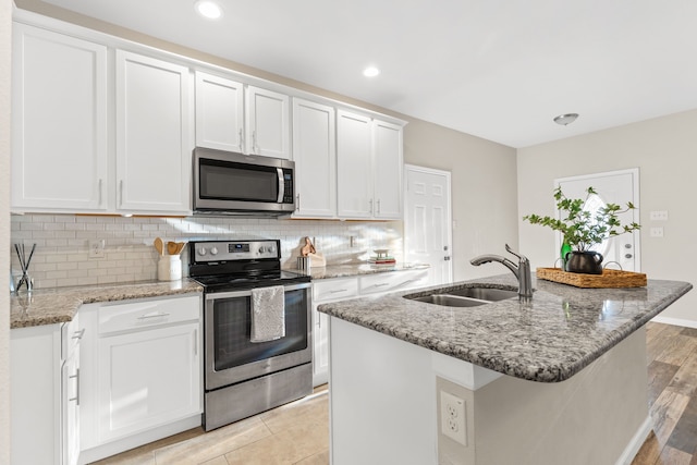 kitchen with appliances with stainless steel finishes, a sink, white cabinets, light stone countertops, and backsplash