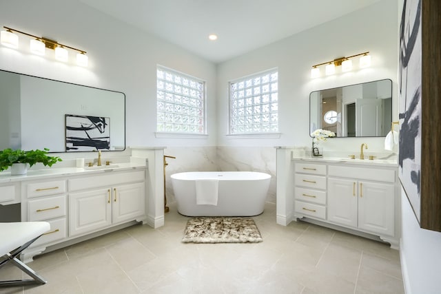 12809 Day Break Trl, Burleson, TX 76028 - full bathroom with two vanities, a freestanding tub, a wainscoted wall, tile walls, and tile patterned flooring