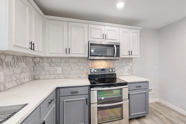 kitchen with appliances with stainless steel finishes, gray cabinets, baseboards, backsplash, and light wood-style floors