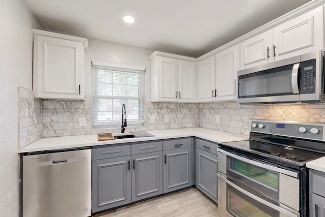 kitchen featuring stainless steel appliances, a sink, gray cabinets, light countertops, and decorative backsplash
