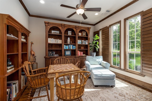 sitting room featuring healthy amount of natural light, wood finished floors, a ceiling fan, crown molding, and baseboards