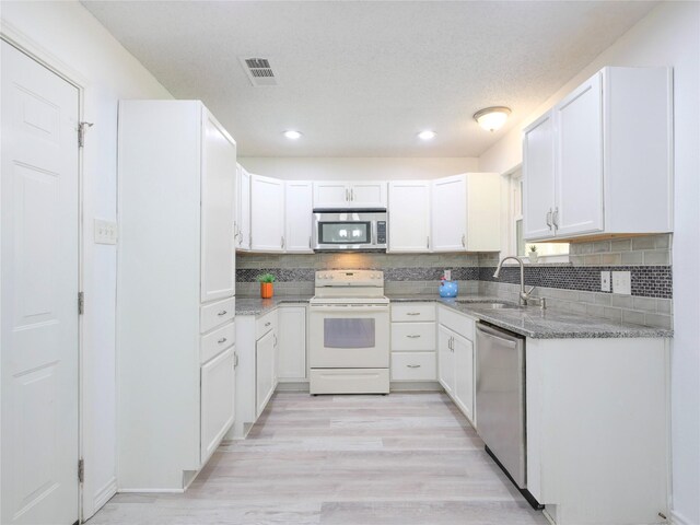 kitchen featuring a sink, appliances with stainless steel finishes, light stone counters, light wood-type flooring, and decorative backsplash