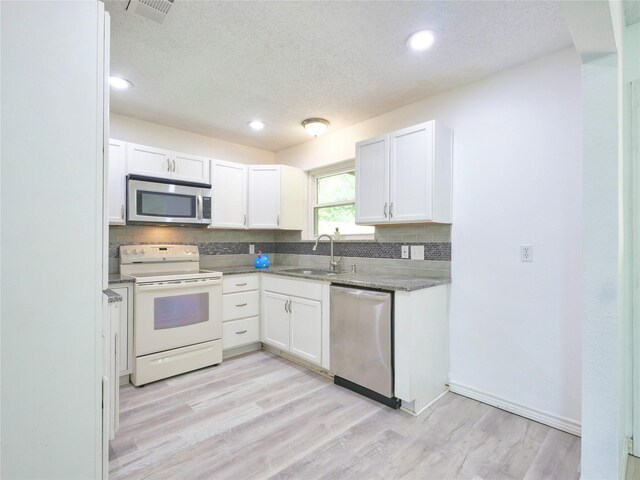 kitchen with appliances with stainless steel finishes, a sink, backsplash, a textured ceiling, and light wood-type flooring
