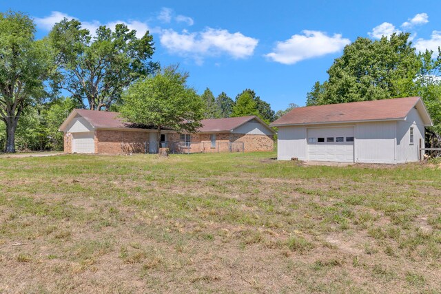 view of green lawn with a detached garage and an outbuilding