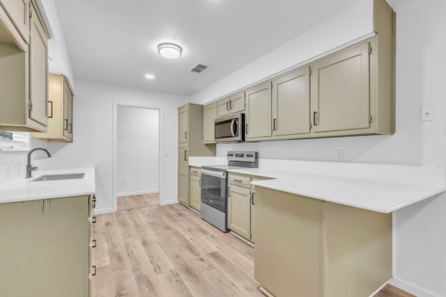 kitchen with appliances with stainless steel finishes, a sink, light wood-type flooring, light countertops, and a peninsula