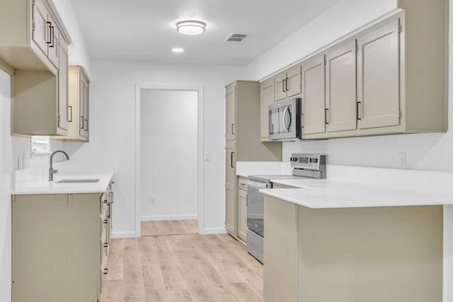 kitchen with stainless steel appliances, a sink, light countertops, light wood-style floors, and gray cabinets