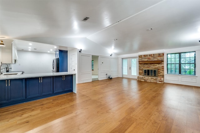 unfurnished living room with a sink, vaulted ceiling, plenty of natural light, light wood-style flooring, and a decorative wall