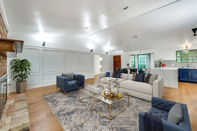 living room featuring light wood-style floors, a decorative wall, and vaulted ceiling