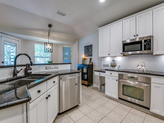 kitchen featuring appliances with stainless steel finishes, a sink, backsplash, light tile patterned flooring, and vaulted ceiling