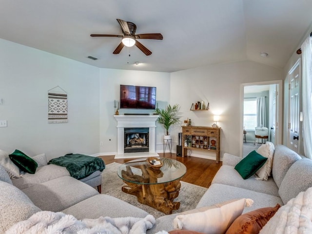 living area featuring ceiling fan, a fireplace with raised hearth, wood finished floors, and vaulted ceiling