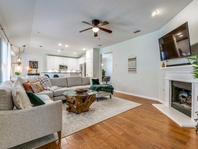 living room with ceiling fan, hardwood / wood-style flooring, baseboards, a fireplace with raised hearth, and recessed lighting