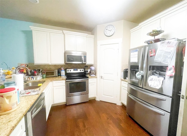kitchen featuring appliances with stainless steel finishes, dark wood-style flooring, a sink, white cabinetry, and decorative backsplash