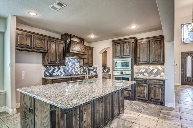 14015 Steadman Dr, Frisco, TX 75035 - kitchen with a sink, arched walkways, appliances with stainless steel finishes, tasteful backsplash, and light stone counters