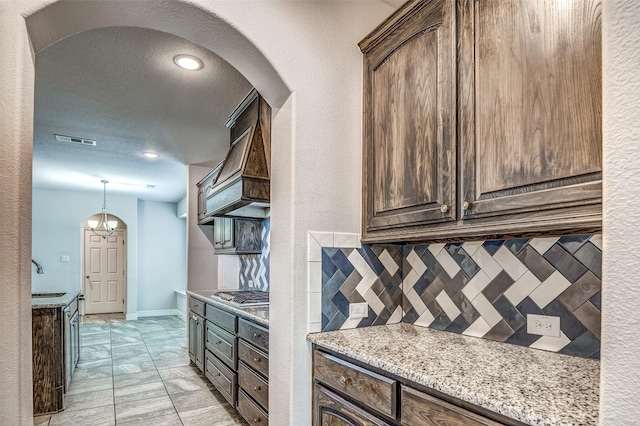 14015 Steadman Dr, Frisco, TX 75035 - kitchen featuring arched walkways, tasteful backsplash, dark brown cabinets, stainless steel gas cooktop, and light stone counters