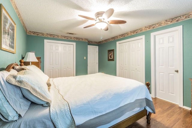 bedroom featuring two closets, wood finished floors, a textured ceiling, and ceiling fan