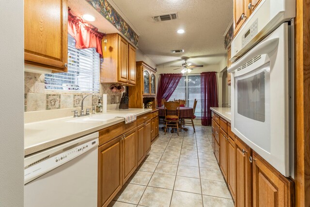 kitchen with white appliances, a sink, a textured ceiling, tasteful backsplash, and brown cabinets