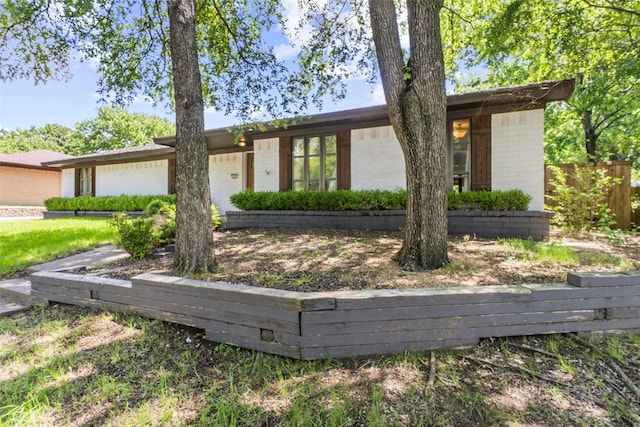 mid-century modern home with an attached garage, brick siding, and fence