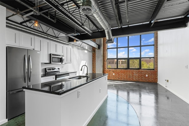 kitchen featuring appliances with stainless steel finishes, brick wall, a sink, baseboards, and a kitchen island with sink