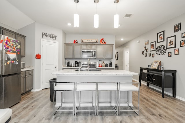 kitchen featuring appliances with stainless steel finishes, light wood finished floors, a breakfast bar area, a kitchen island with sink, and baseboards