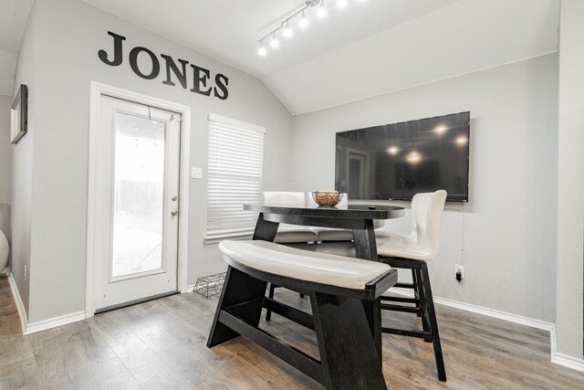 dining space featuring wood finished floors, baseboards, vaulted ceiling, and track lighting