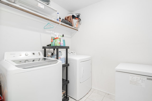 clothes washing area featuring independent washer and dryer, light tile patterned floors, and baseboards