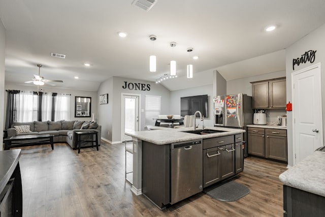 kitchen featuring stainless steel appliances, vaulted ceiling, a sink, light countertops, and dark wood-style floors