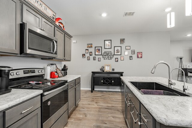kitchen with stainless steel appliances, a sink, light wood-style flooring, recessed lighting, and decorative light fixtures