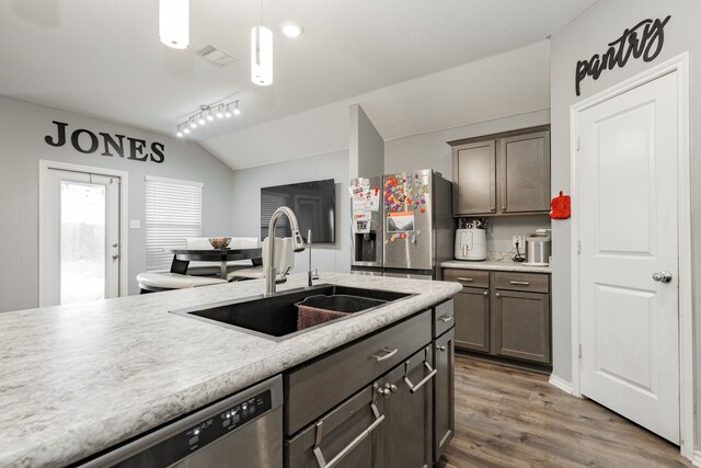 kitchen featuring stainless steel appliances, a sink, vaulted ceiling, wood finished floors, and light countertops