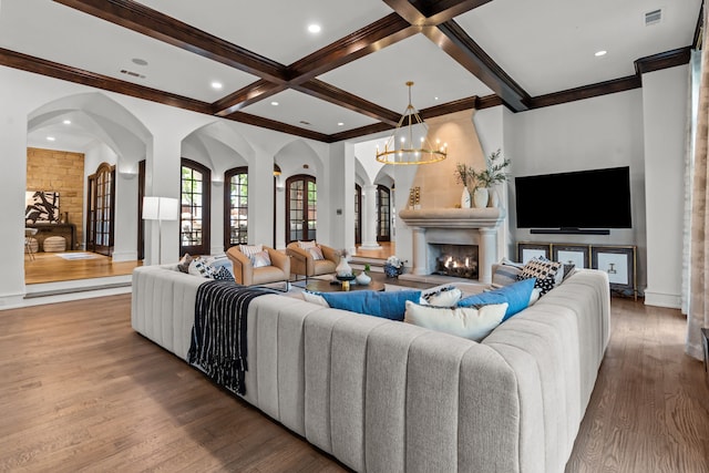 living room with wood finished floors, beam ceiling, coffered ceiling, arched walkways, and a chandelier