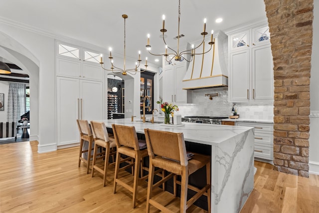 1100 La Paloma Ct, Southlake, TX 76092 - kitchen featuring arched walkways, a center island with sink, custom exhaust hood, light wood finished floors, and decorative backsplash