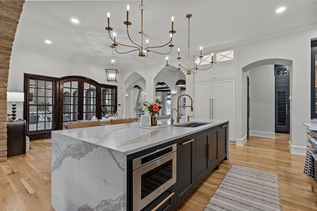 1100 La Paloma Ct, Southlake, TX 76092 - kitchen with arched walkways, stainless steel microwave, a sink, light wood-style floors, and a center island with sink