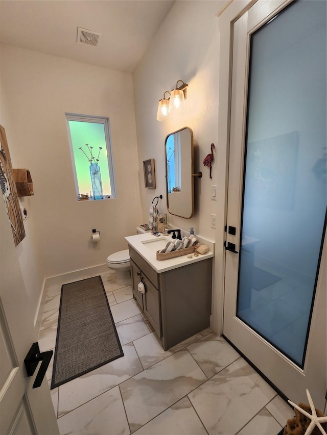 bathroom featuring marble look tile flooring, toilet, vanity, and baseboards