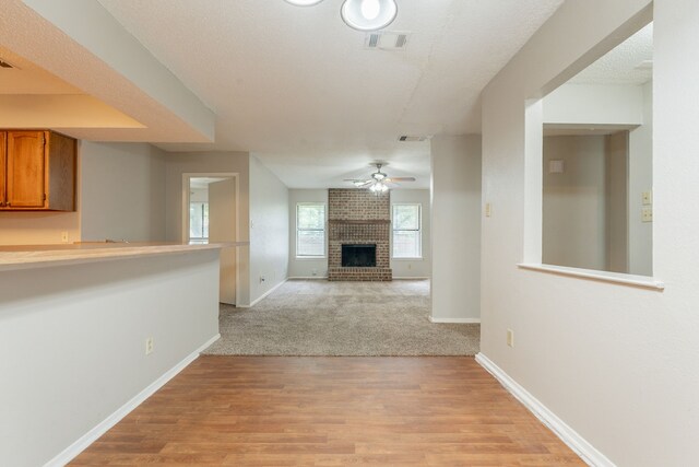 unfurnished living room with ceiling fan, a brick fireplace, baseboards, and light wood finished floors