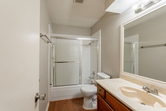 bathroom with wood finished floors, toilet, vanity, shower / bath combination with glass door, and a textured ceiling