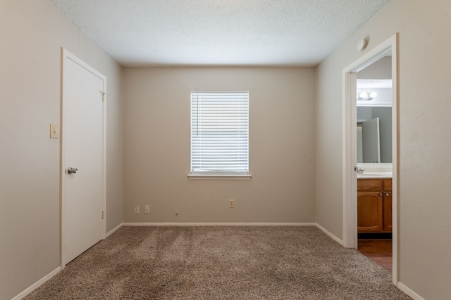 unfurnished bedroom with carpet flooring, a textured ceiling, a sink, ensuite bathroom, and baseboards