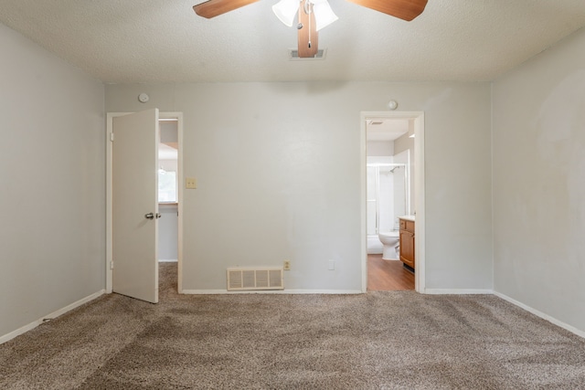 unfurnished bedroom with carpet, a textured ceiling, baseboards, ensuite bathroom, and a ceiling fan