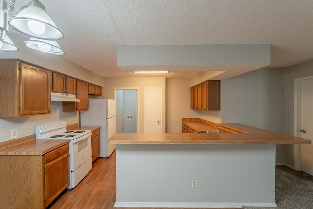 kitchen with white appliances, under cabinet range hood, brown cabinets, light countertops, and a textured ceiling