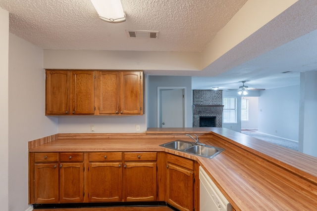 kitchen featuring a sink, a textured ceiling, a fireplace, white dishwasher, and light countertops