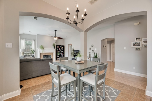 dining area featuring vaulted ceiling, light tile patterned flooring, arched walkways, a glass covered fireplace, and a ceiling fan
