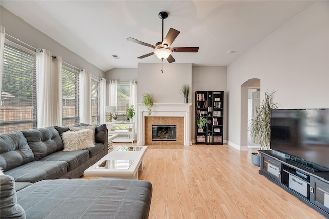 living area featuring ceiling fan, vaulted ceiling, wood finished floors, arched walkways, and a tiled fireplace